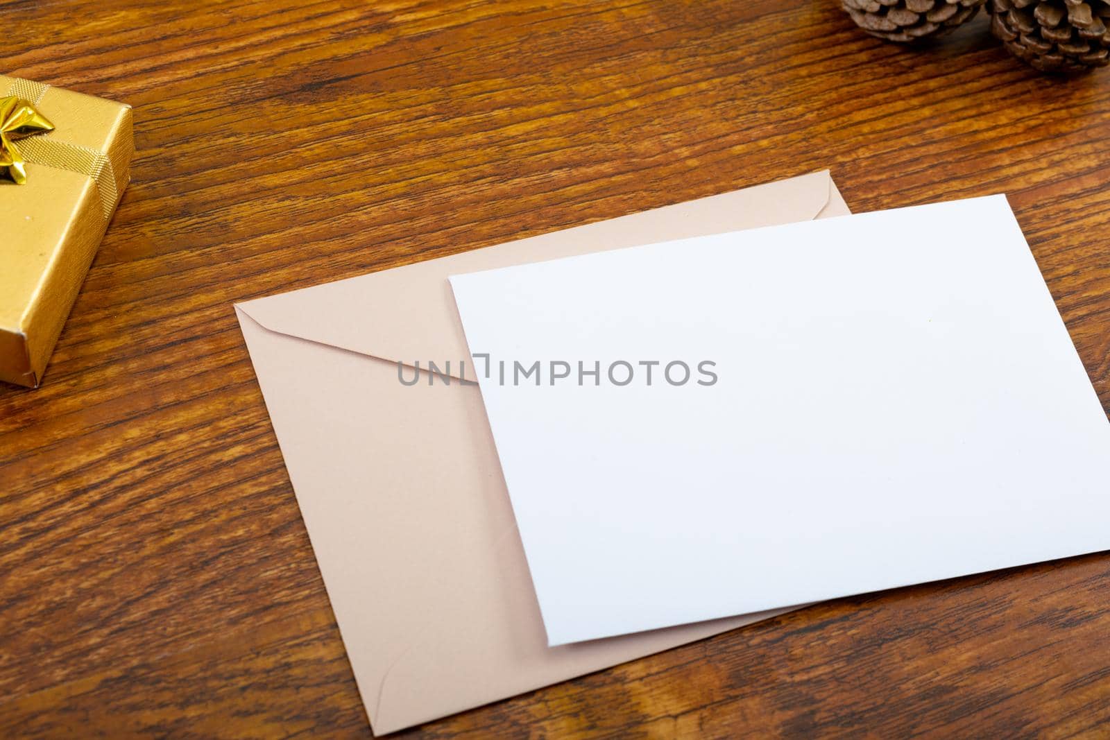 Composition of white card with copy space, envelope and pine cones on wooden background. christmas, communication, tradition and celebration concept.
