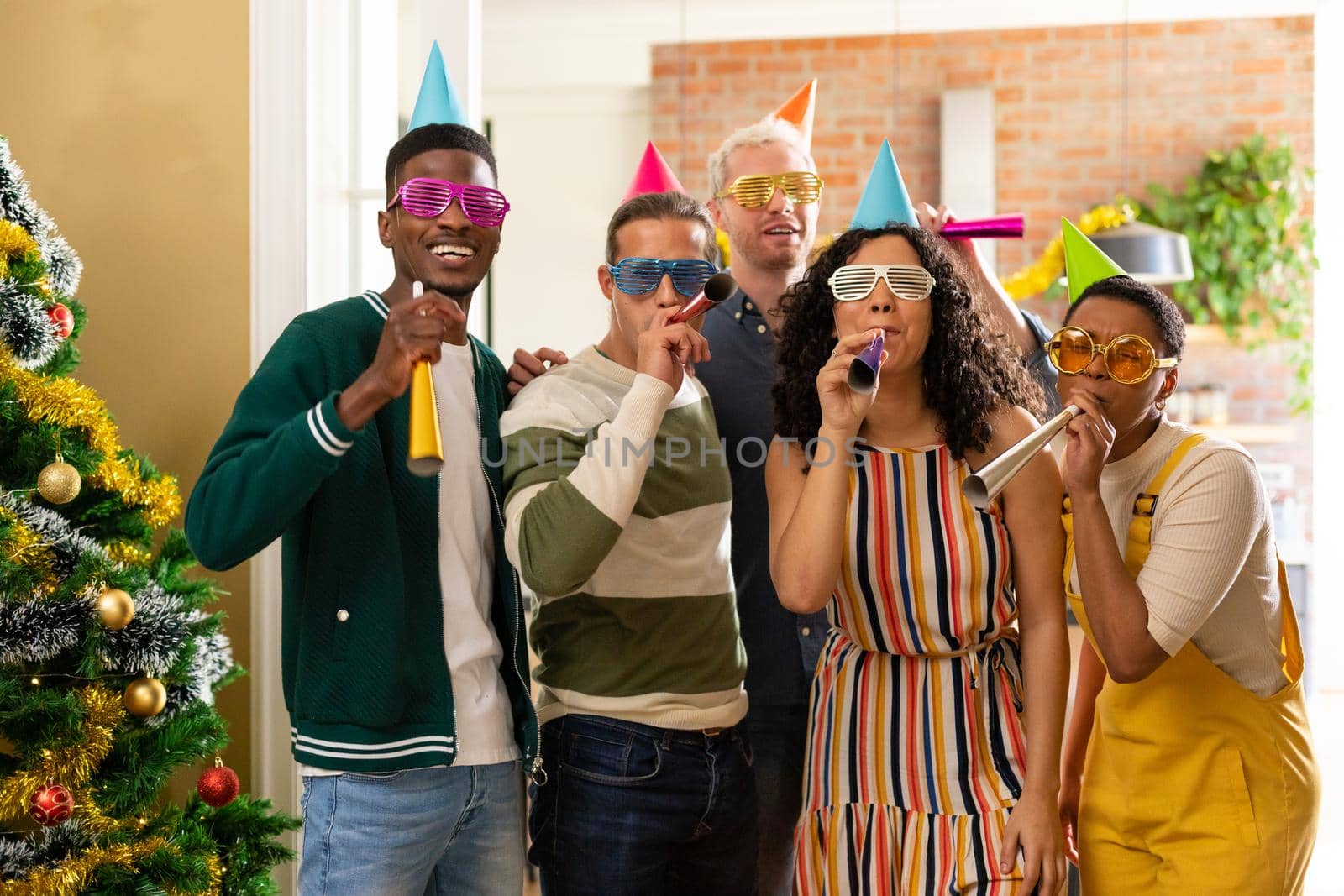 Group of happy diverse female and male friends with whistles and colorful hats celebrating new year by Wavebreakmedia