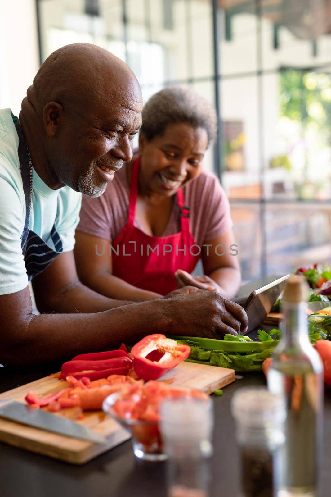 Happy african american senior couple cooking together in kitchen, using tablet by Wavebreakmedia