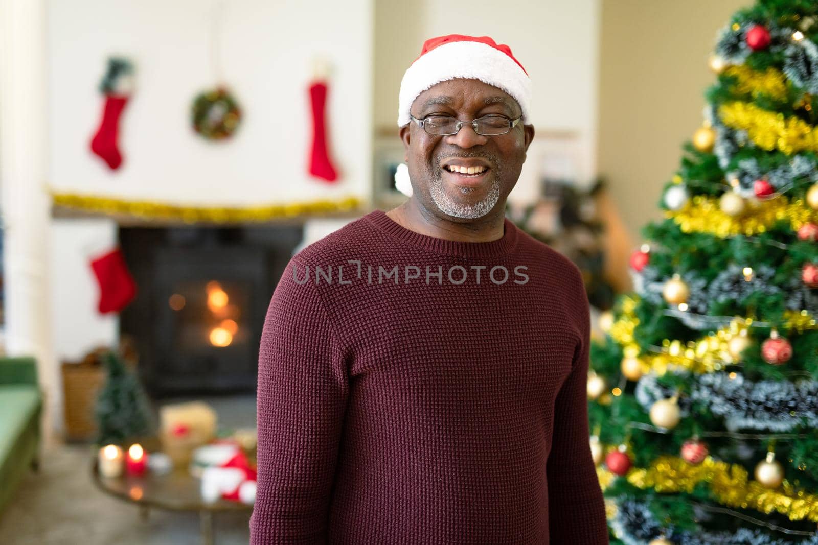 Happy african american senior man in santa hat looking at camera at christmas time. retirement lifestyle and christmas festivities, celebrating at home.