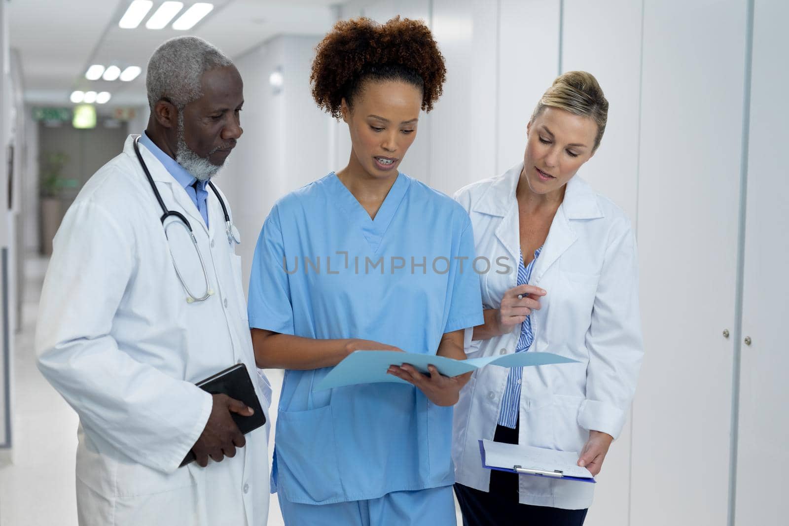 Three diverse male and female doctors standing in hospital corridor looking at medical documentation by Wavebreakmedia