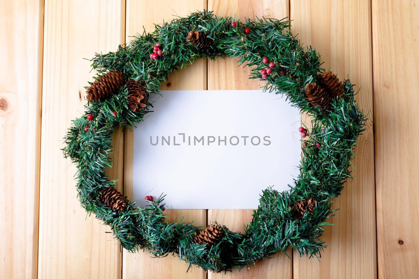 Composition of white card with copy space framed with wreath on wooden background. christmas, tradition and celebration concept.