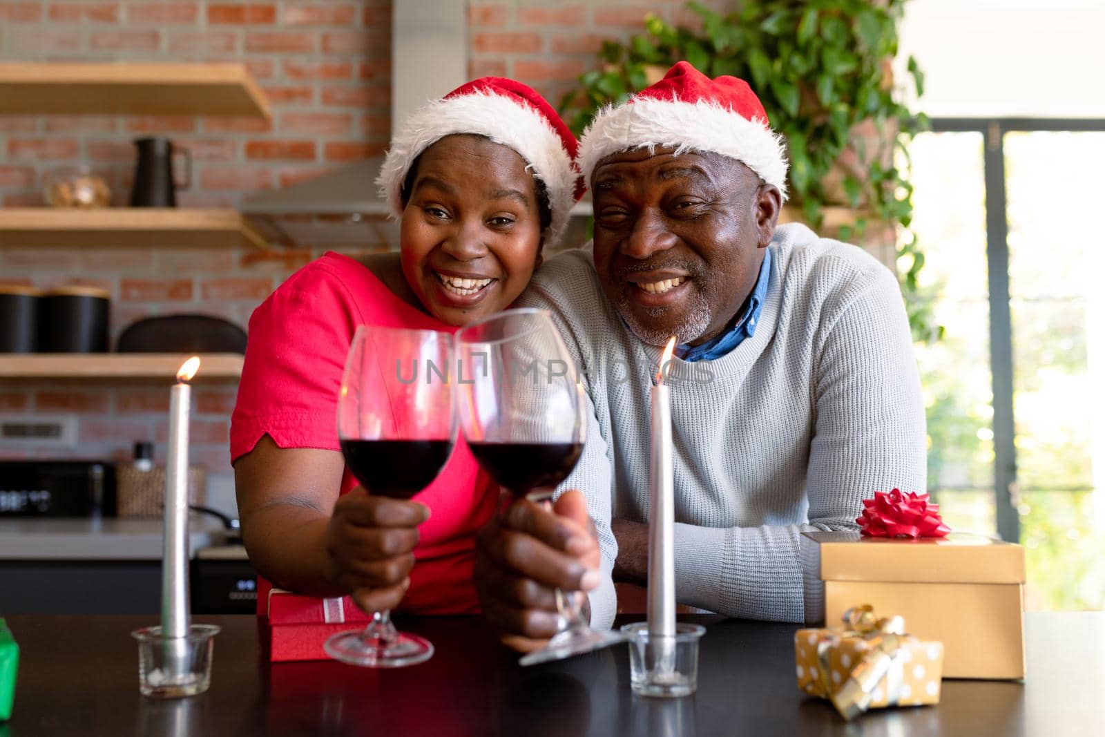 Happy african american senior couple with vine having video call in kitchen at christmas time. retirement lifestyle, christmas festivities and communication technology.