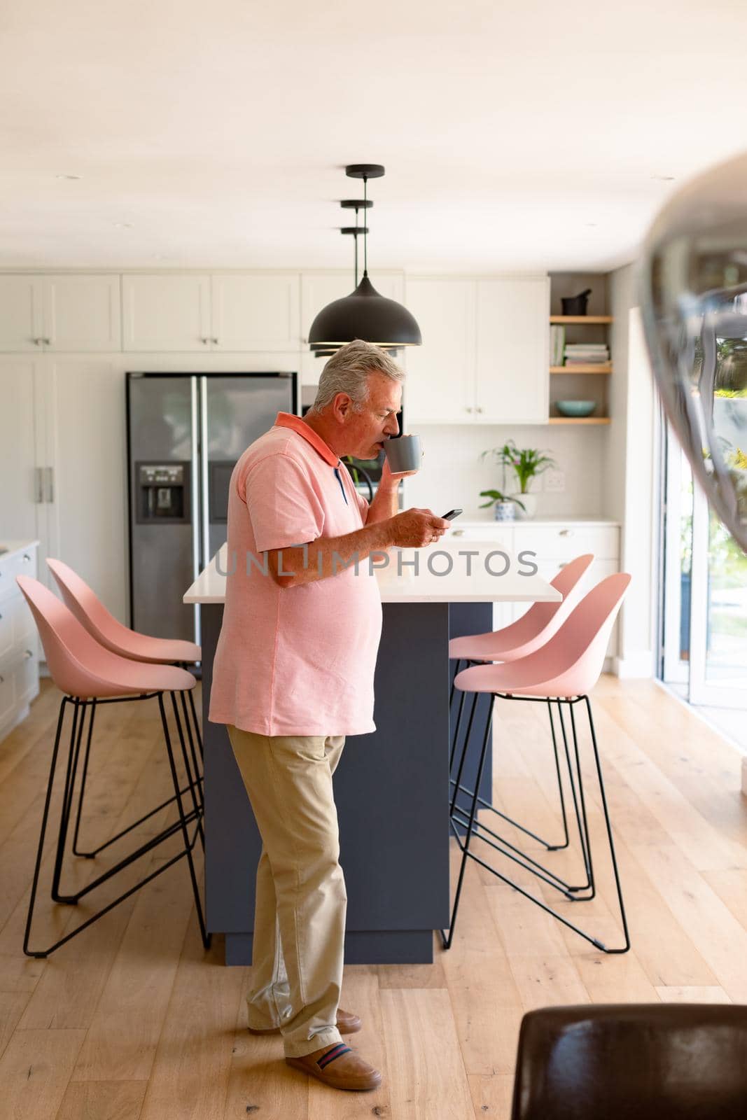 Relaxed caucasian senior man standing in kitchen, drinking coffee and using smartphone by Wavebreakmedia