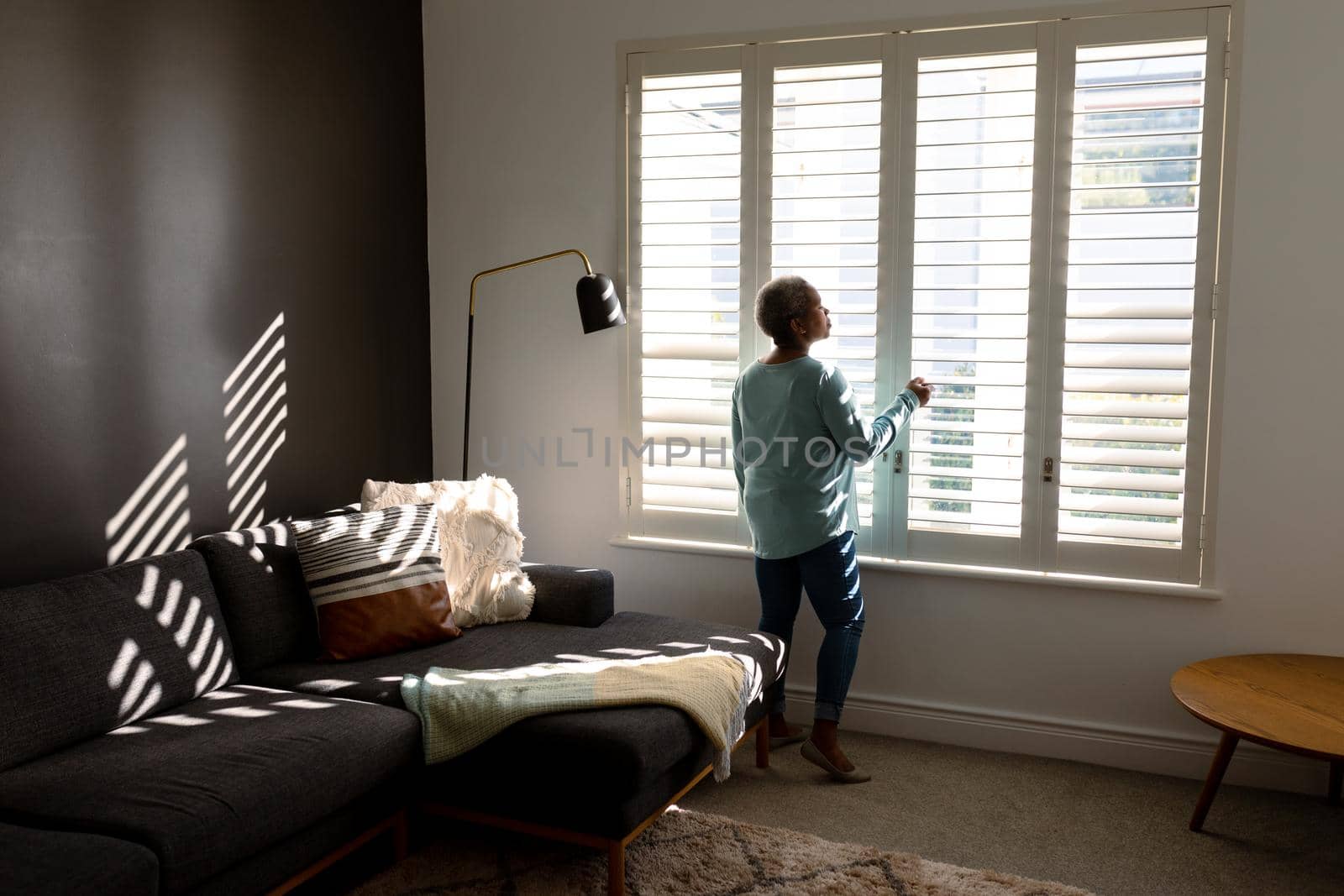 African american senior woman standing at window and looking into distance. retirement lifestyle, spending time at home and garden.