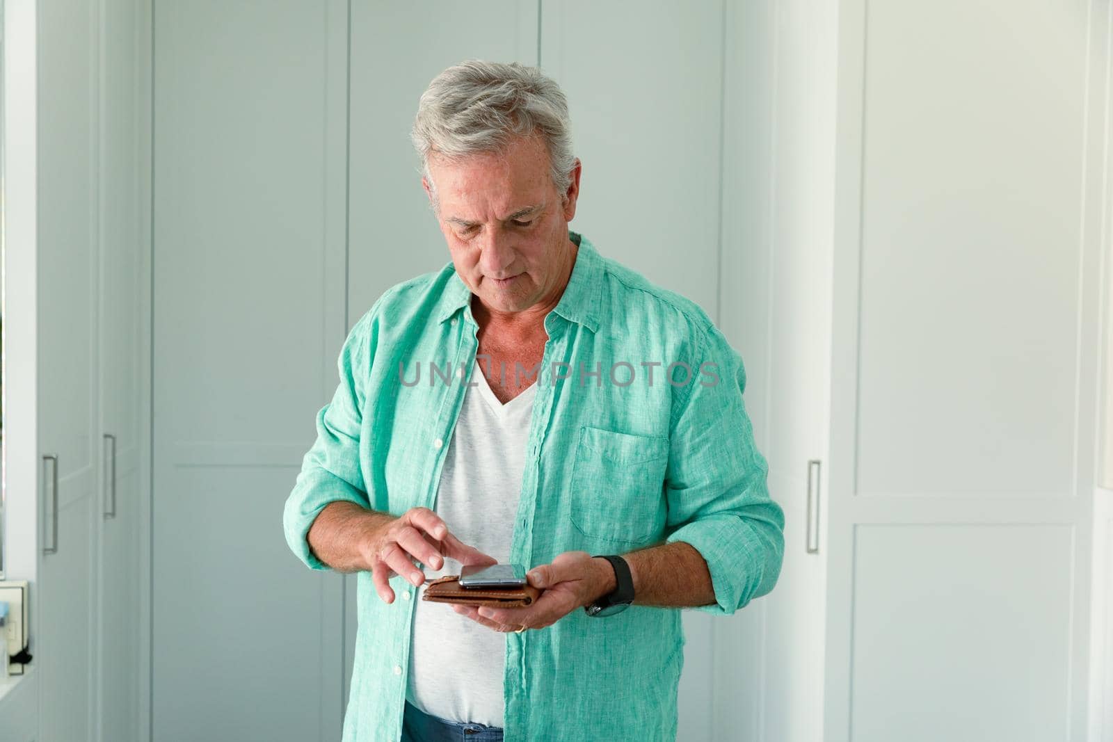 Caucasian senior man holding smartphone and documents in bedroom. travel preparation during covid 19 pandemic.