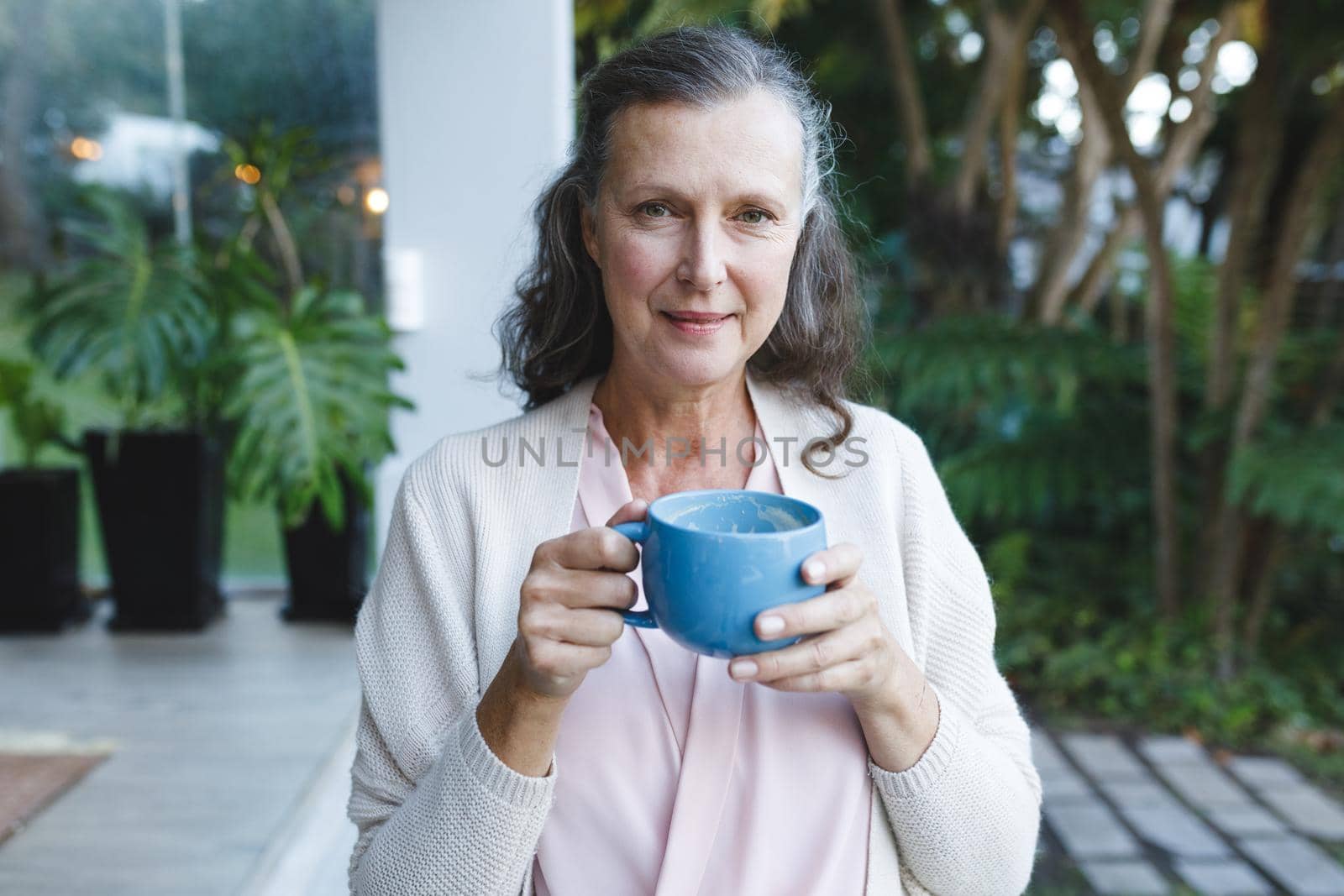Portrait of happy senior caucasian woman looking to camera, holding cup in garden by Wavebreakmedia