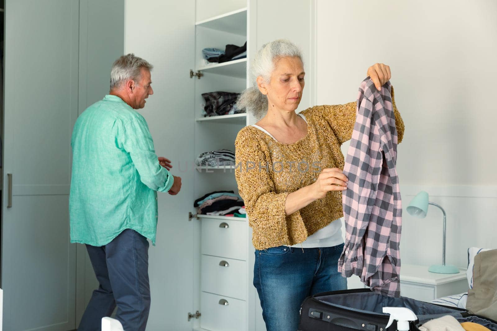 Focused caucasian senior couple packing suitcase together in bedroom by Wavebreakmedia