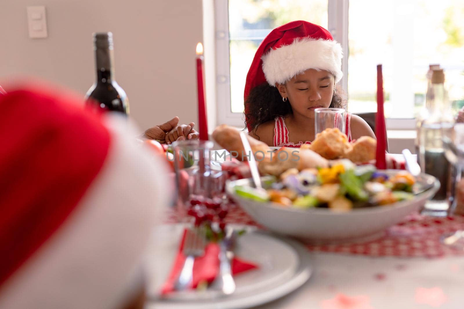 African american girl wearing santa hat praying at christmas table by Wavebreakmedia