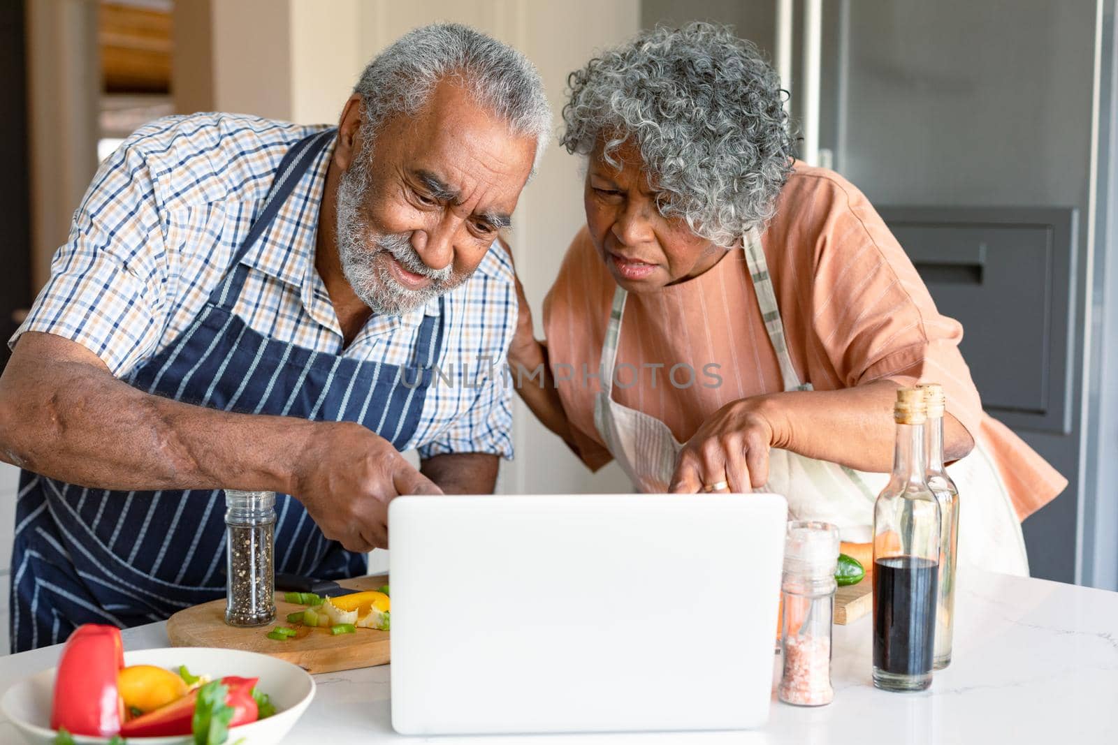 Happy arfican american senior couple preparing meal together and using laptop. healthy retirement lifestyle at home.