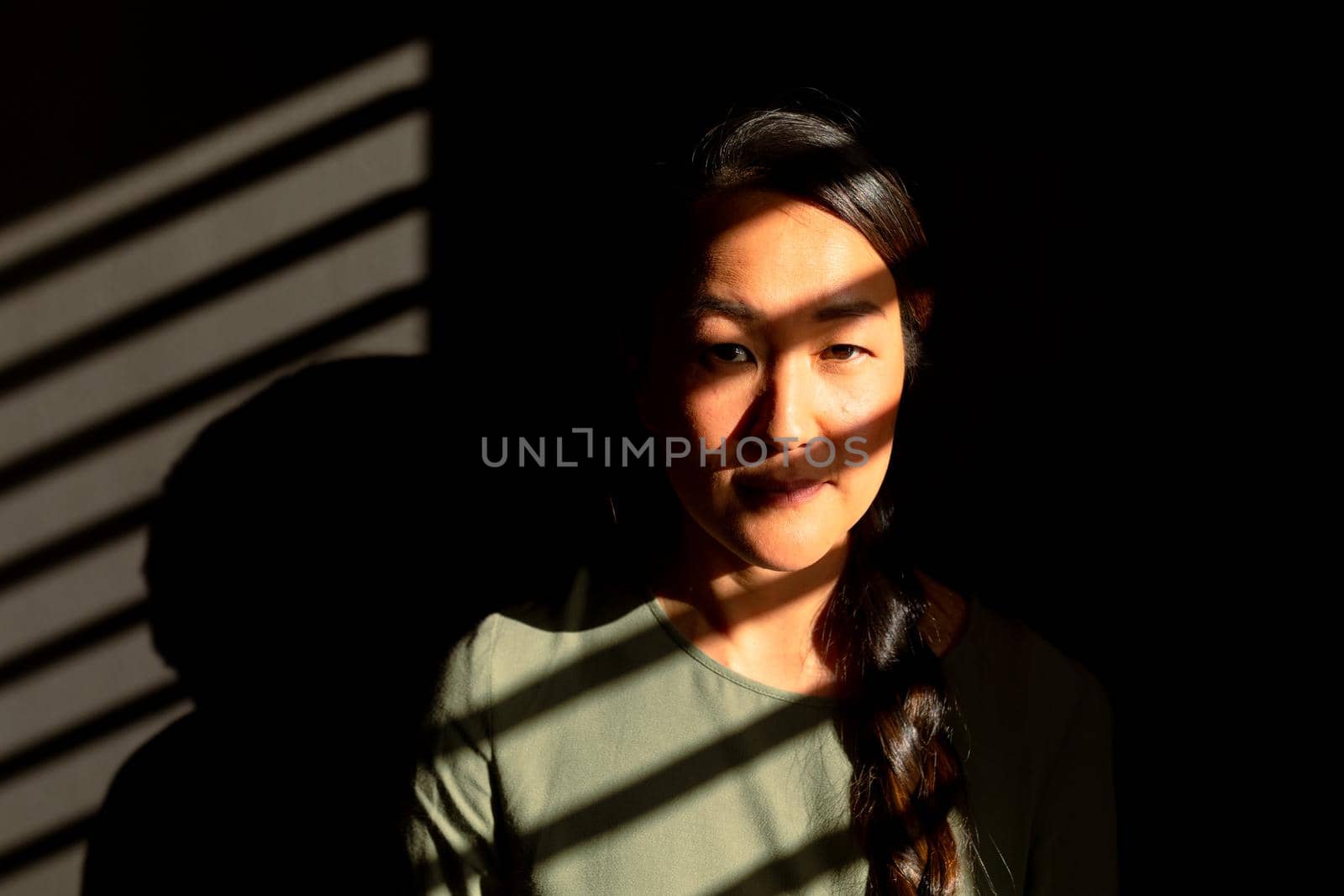 Portrait of serious asian woman standing in ray of light at home by Wavebreakmedia