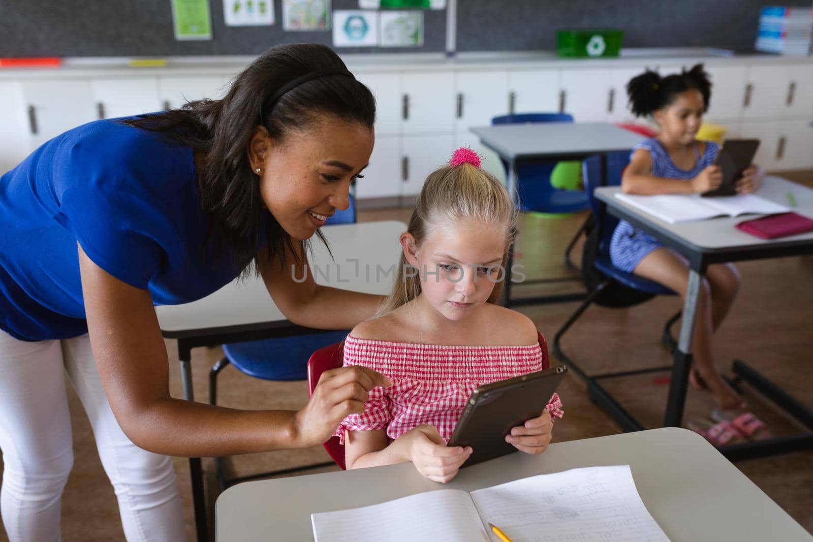 African american female teacher teaching a girl to use digital tablet in class at elementary school. education back to school health safety during covid19 coronavirus pandemic