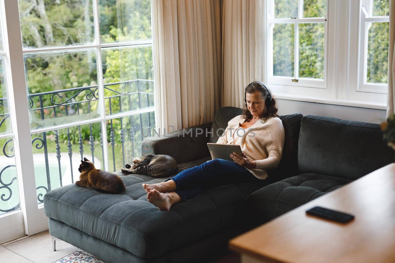 Happy senior caucasian woman in living room sitting on sofa, wearing headphones, using tablet by Wavebreakmedia
