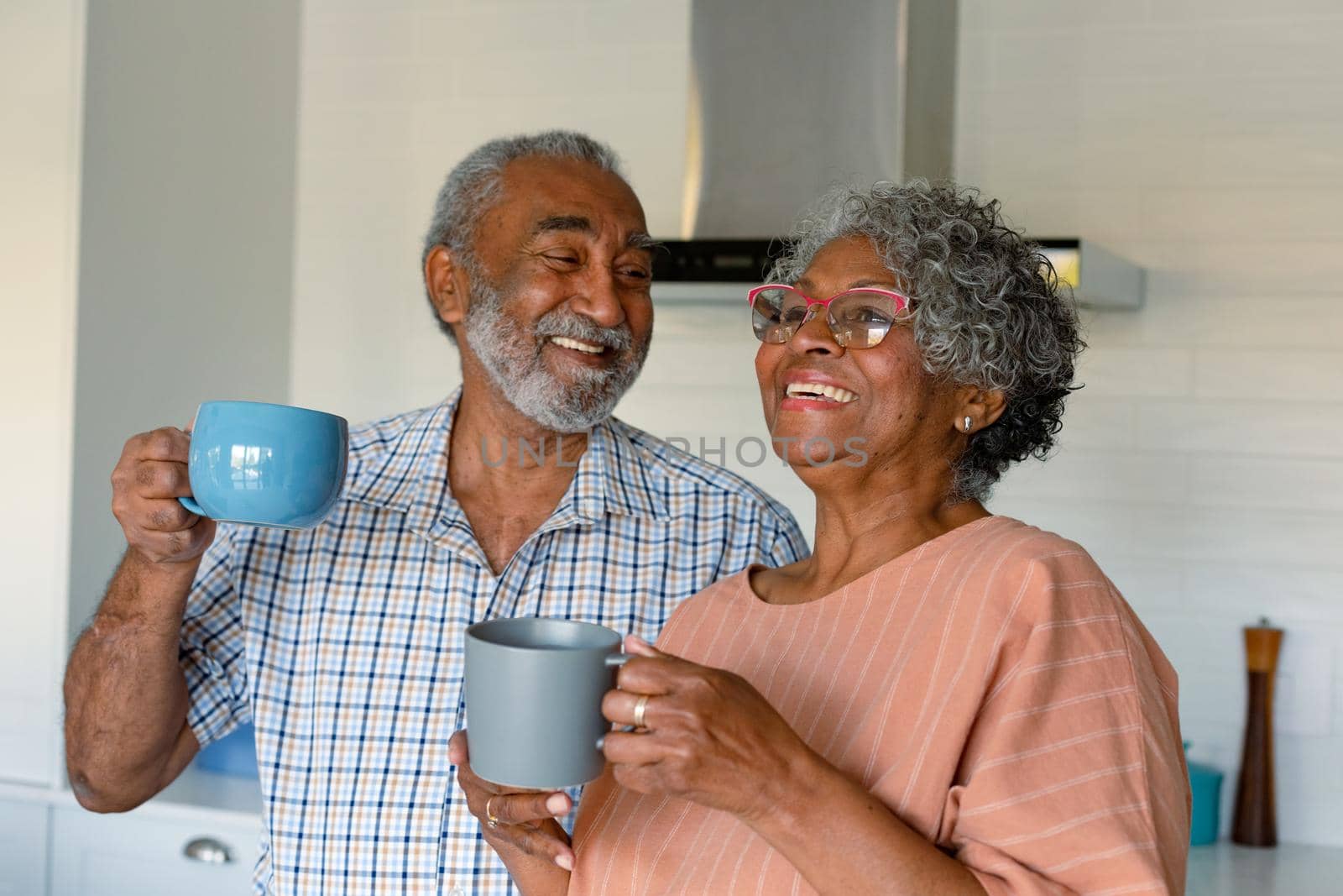 Happy african american senior couple holding mugs with coffee and talking by Wavebreakmedia