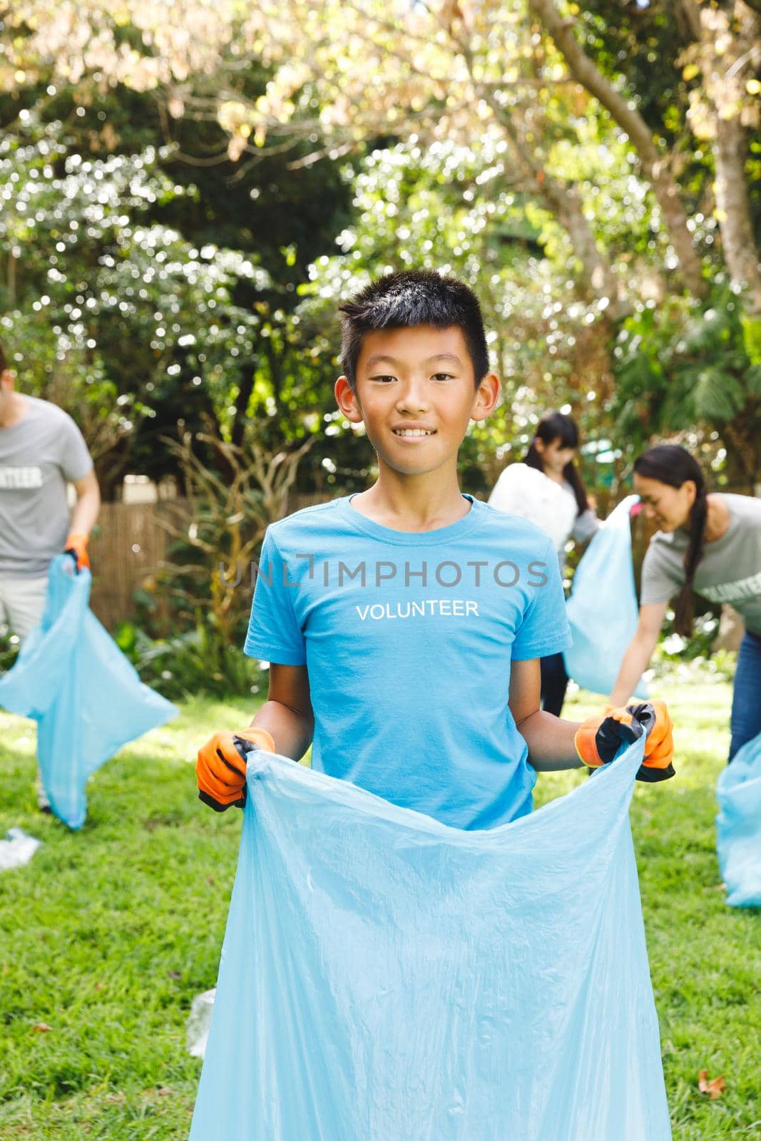 Portrait of smiling asian son, collecting rubbish in sacks with family in the countryside. eco conservation volunteers, countryside clean-up.