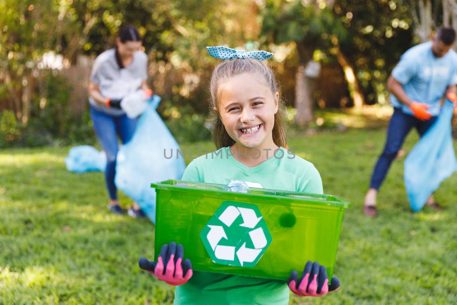 Portrait of smiling caucasian daughter holding recycling box, cleaning up countryside with parents. eco conservation volunteers, countryside clean-up.