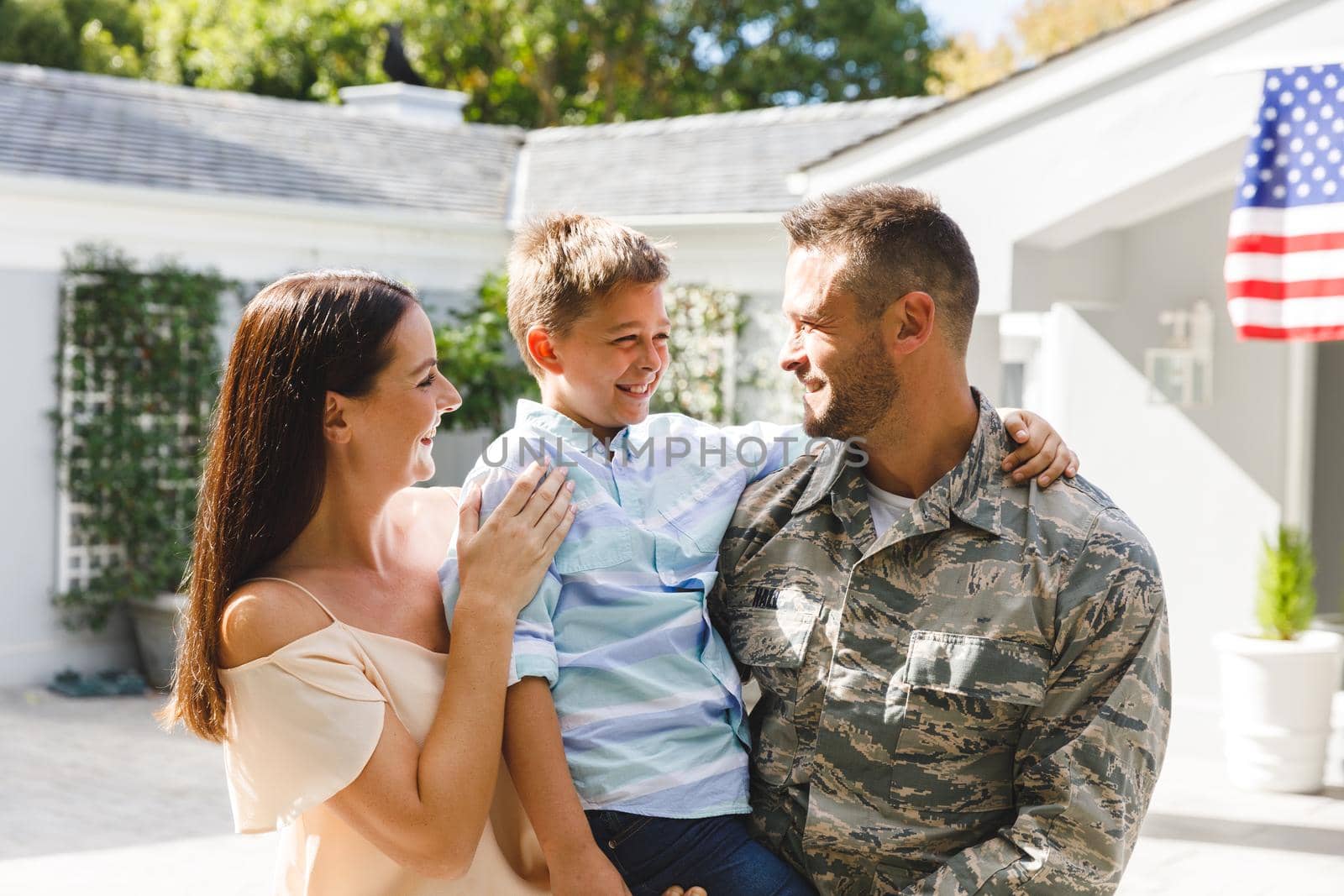 Smiling caucasian male soldier with son and wife outside house decorated with american flag. soldier returning home to family.