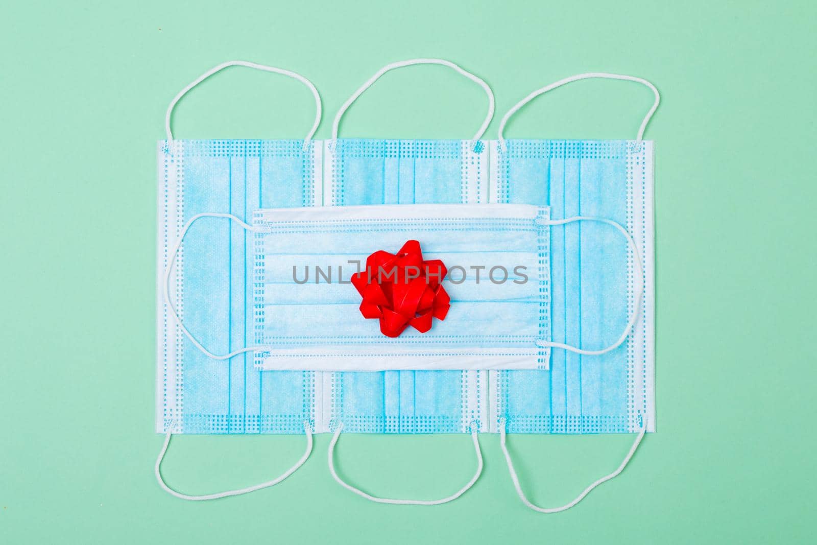 Composition of face masks with red ribbon on green background. christmas, tradition and celebration during coronavirus pandemic concept.
