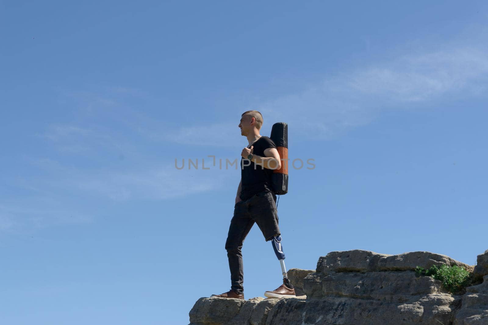 a man on a prosthetic leg travels the mountains. Dressed in black jeans and a T-shirt, he carrying mat.