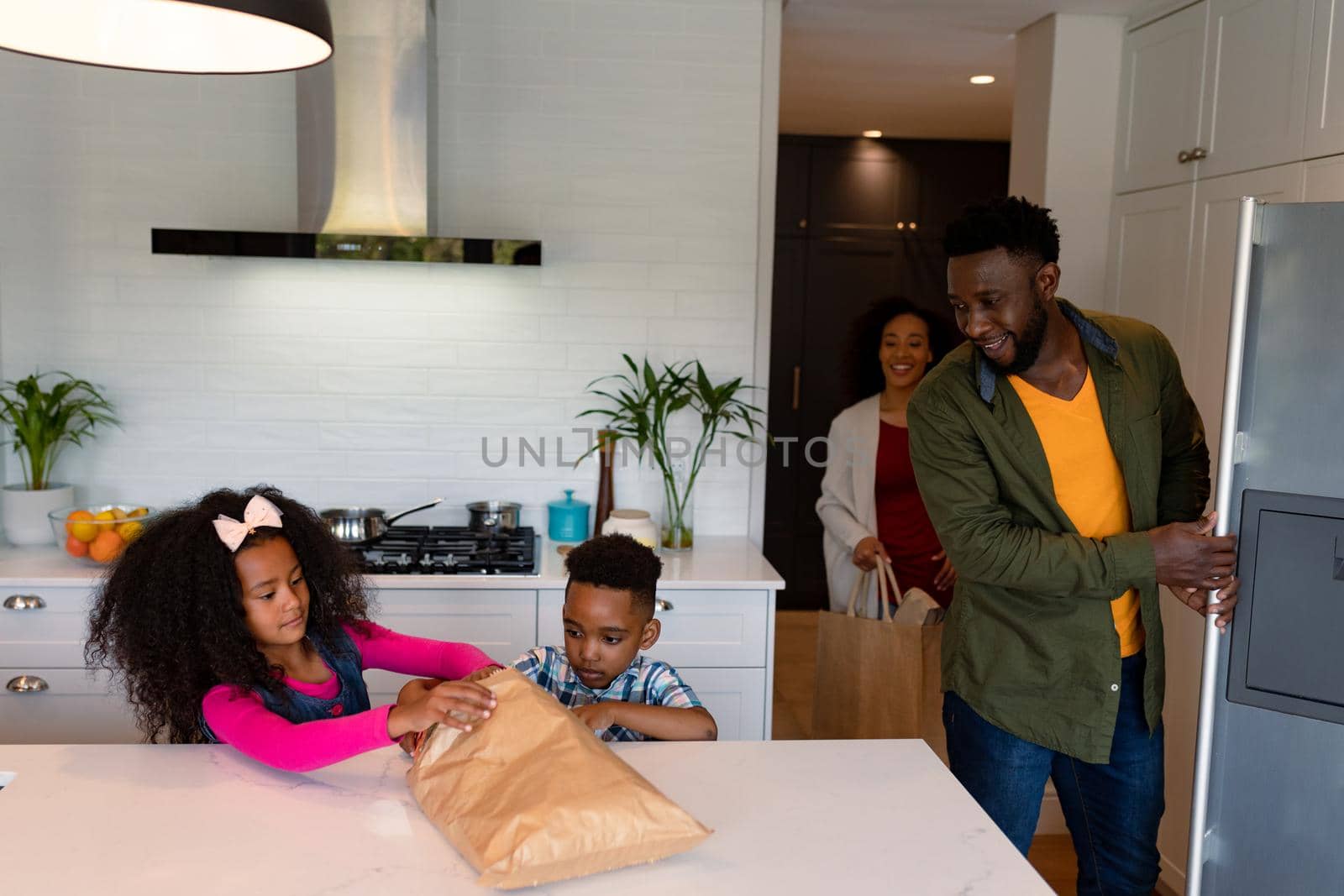 Happy african american siblings unpacking groceries with parents in kitchen. family time, having fun together at home.