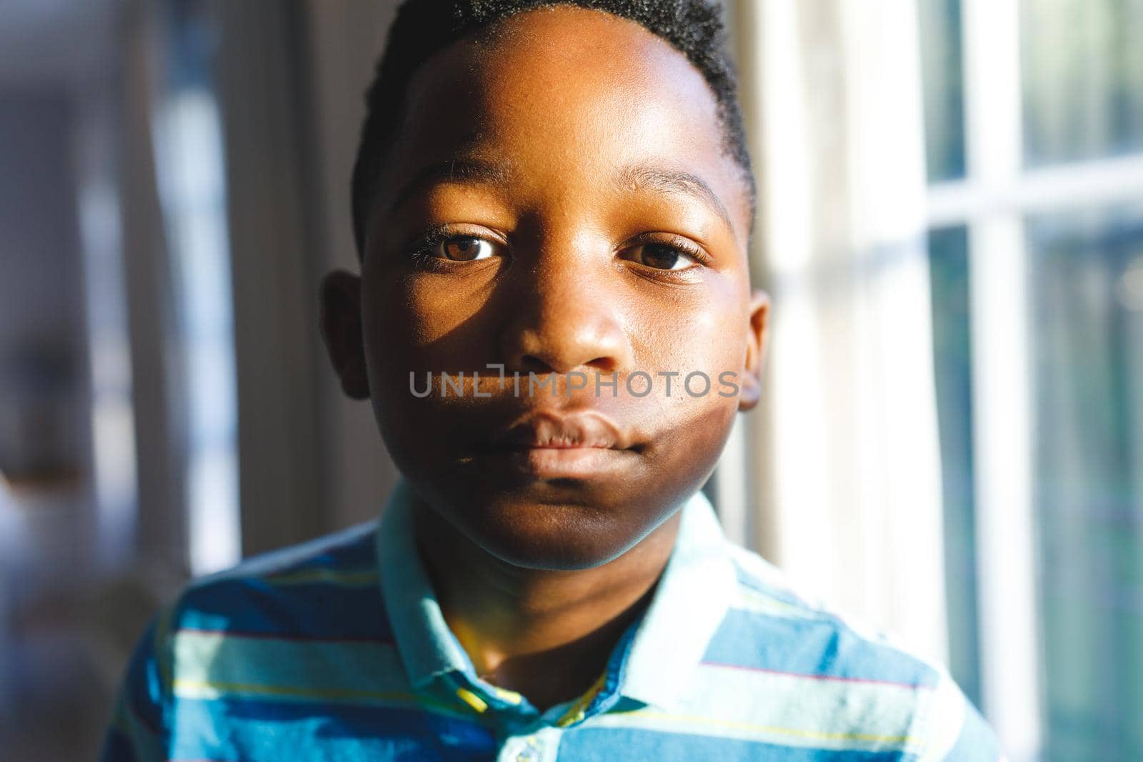 Portrait of african american boy looking at camera in sunny living room. spending time alone at home.