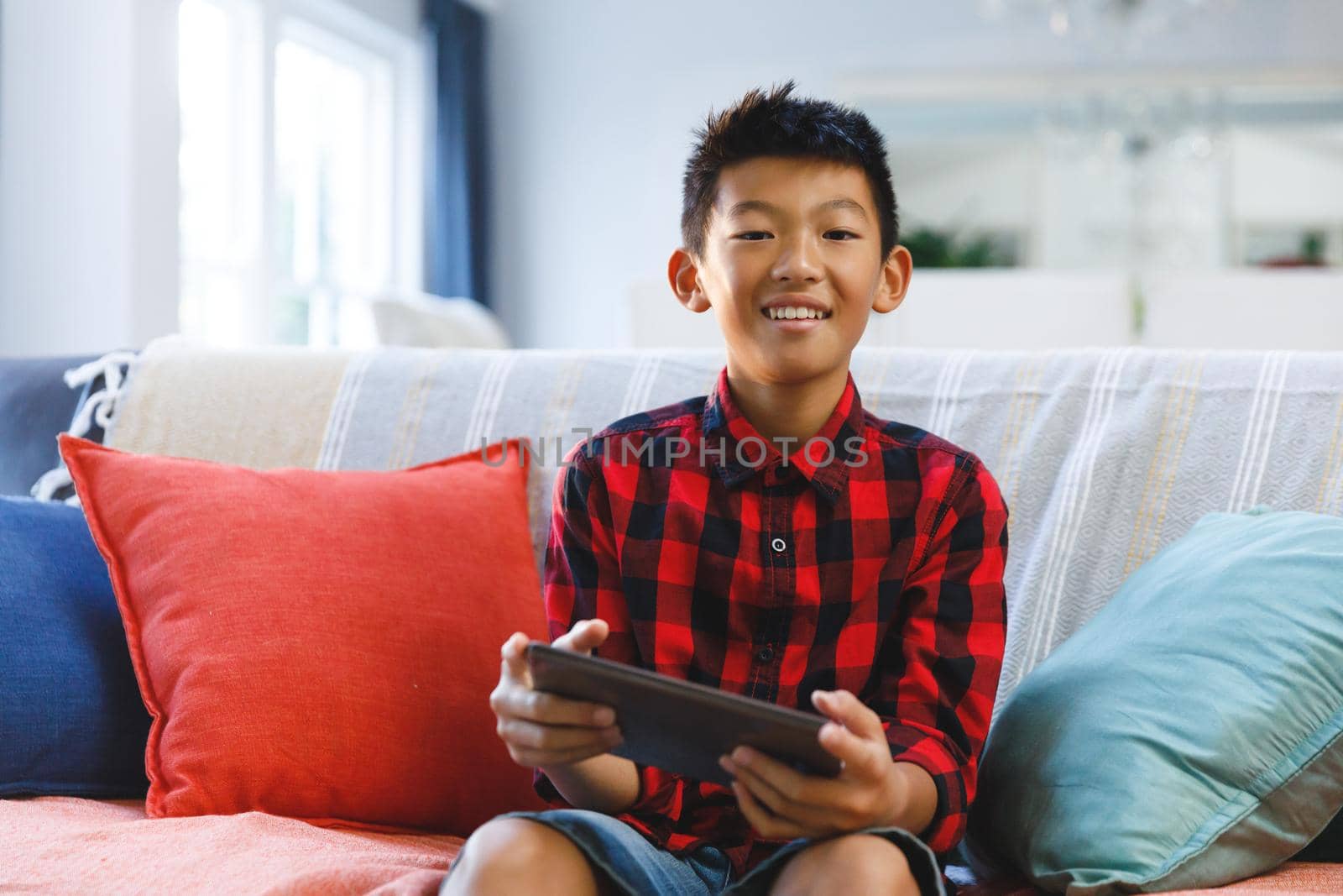 Portrait of smiling asian boy sitting on couch and using tablet by Wavebreakmedia