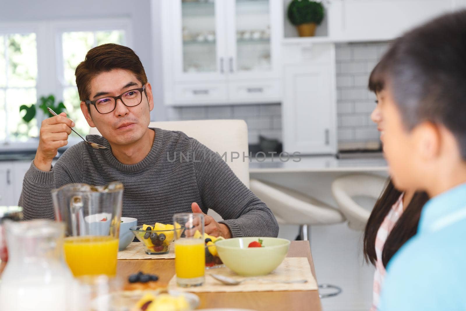 Asian father with son and daughter sitting at table having conversation at breakfast by Wavebreakmedia