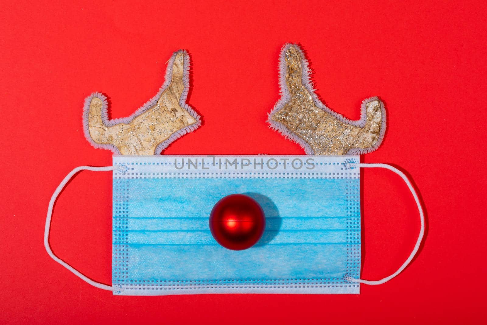 Composition of face mask with christmas decorations in shape of reindeer on green background. christmas, tradition and celebration during coronavirus pandemic concept.