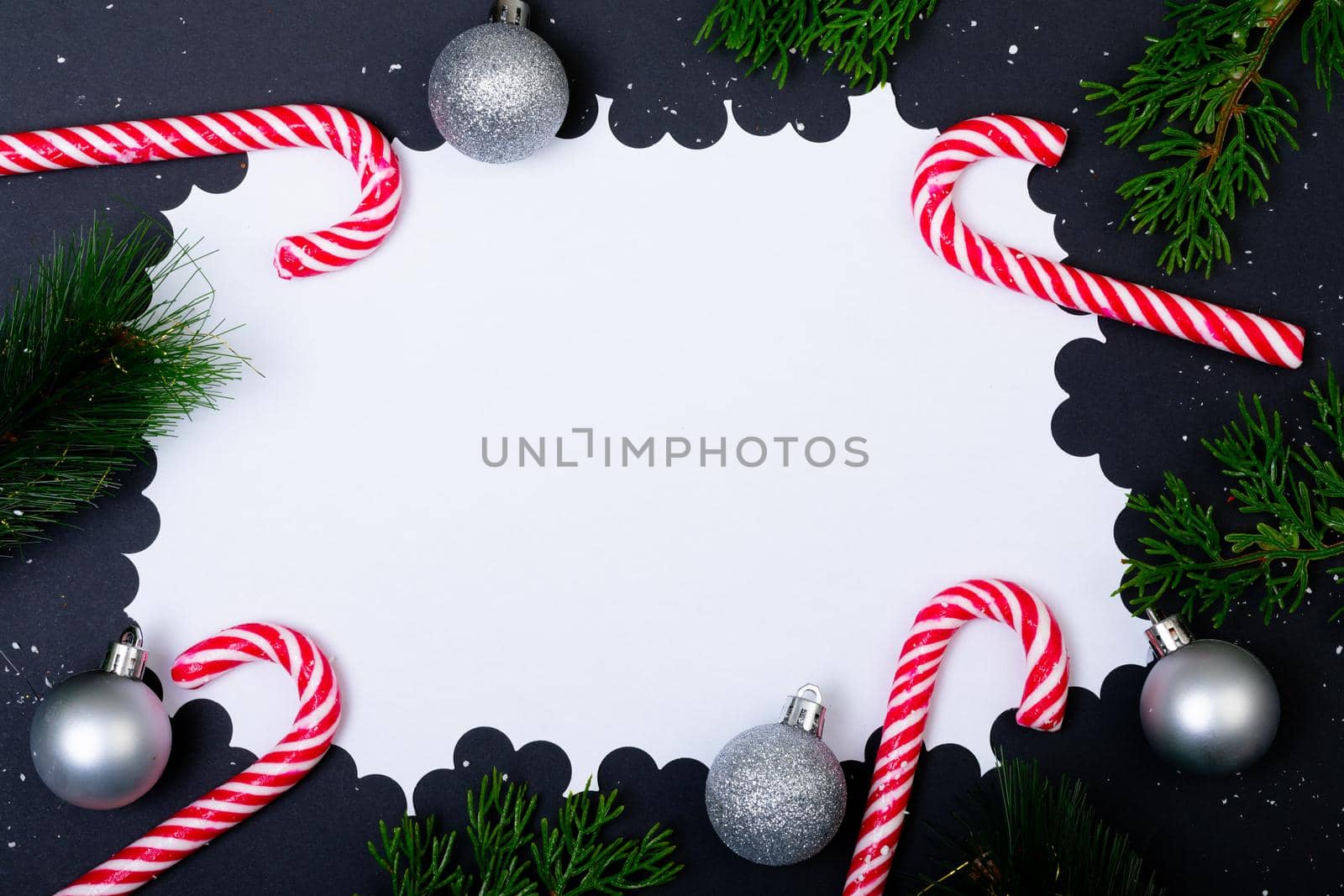 Composition of card with copy space framed with tree branches and candy canes on black background. christmas, tradition and celebration concept.