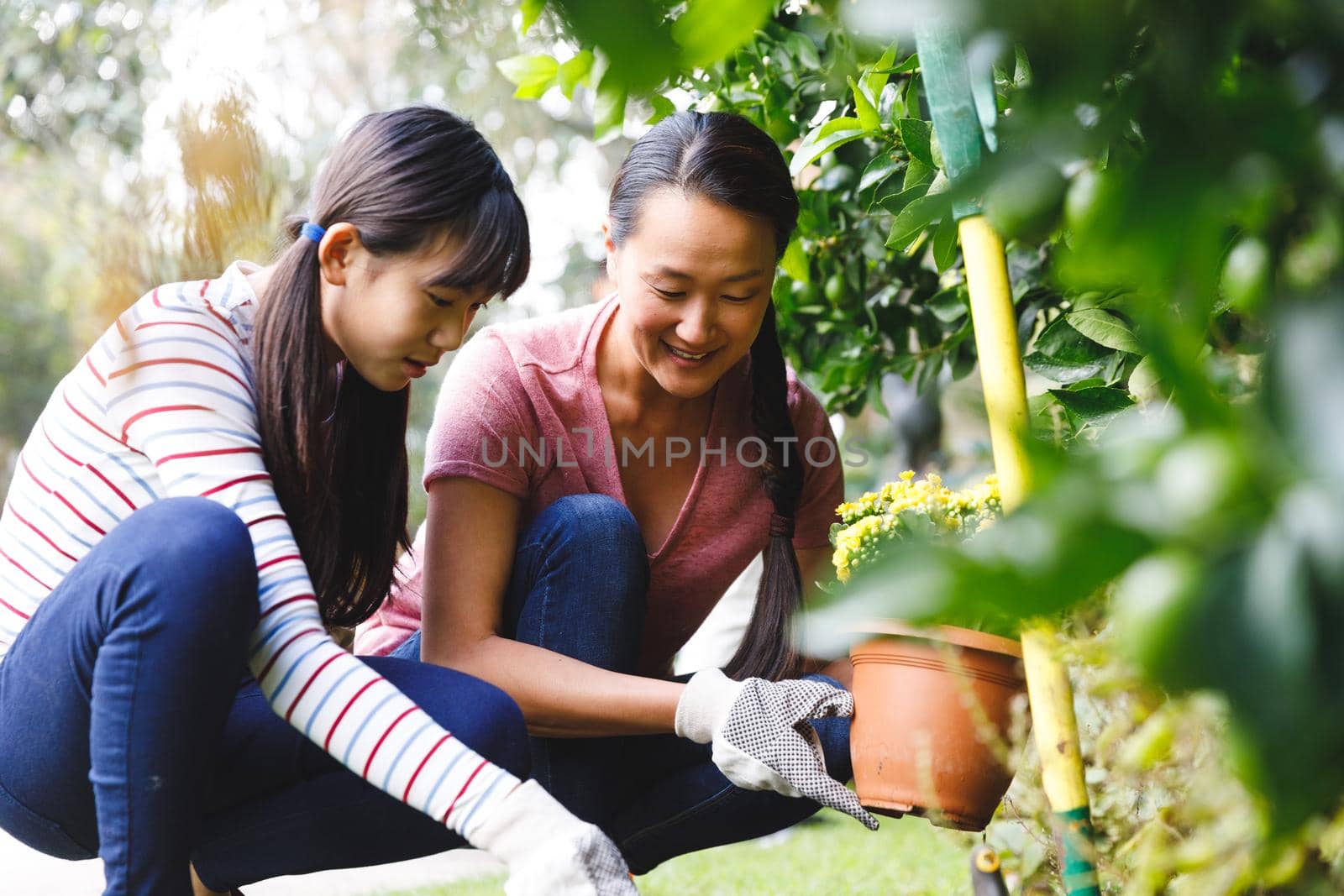 Happy asian mother and daughter smiling, wearing gloves and working in garden. family leisure time at home gardening.