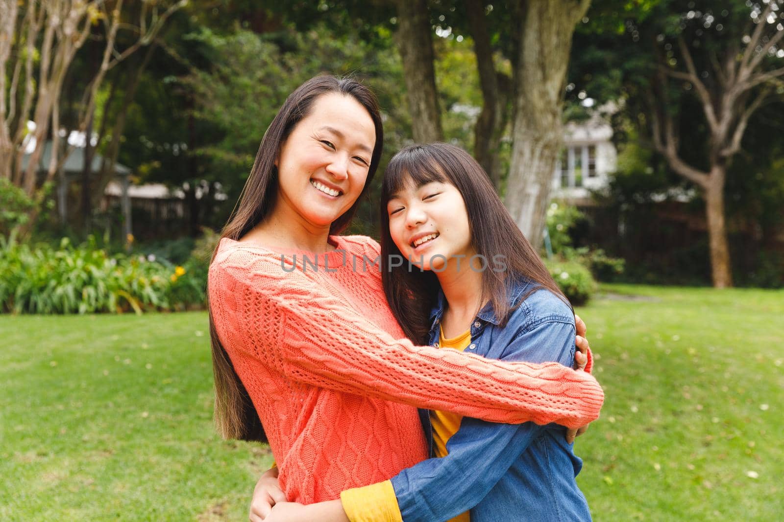 Portrait of happy asian mother embracing her daughter and smiling outdoors in garden. family enjoying leisure time together at home.