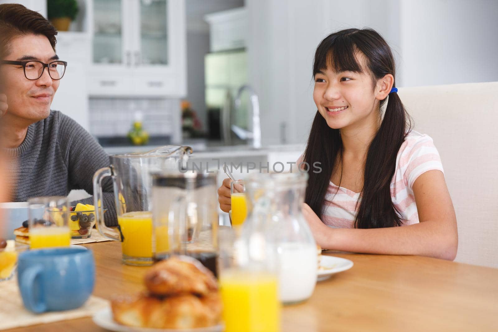 Smiling asian father with daughter sitting at table and having breakfast. family enjoying mealtime together at home.