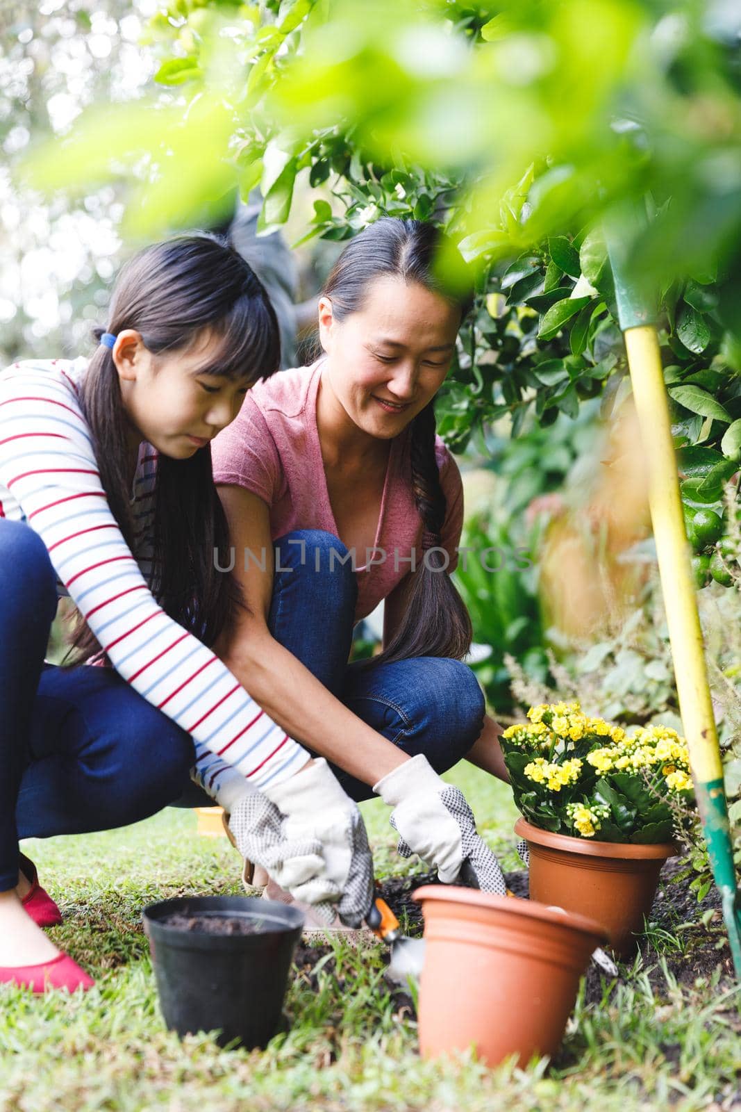 Happy asian mother and daughter smiling, wearing gloves and working in garden. family leisure time at home gardening.