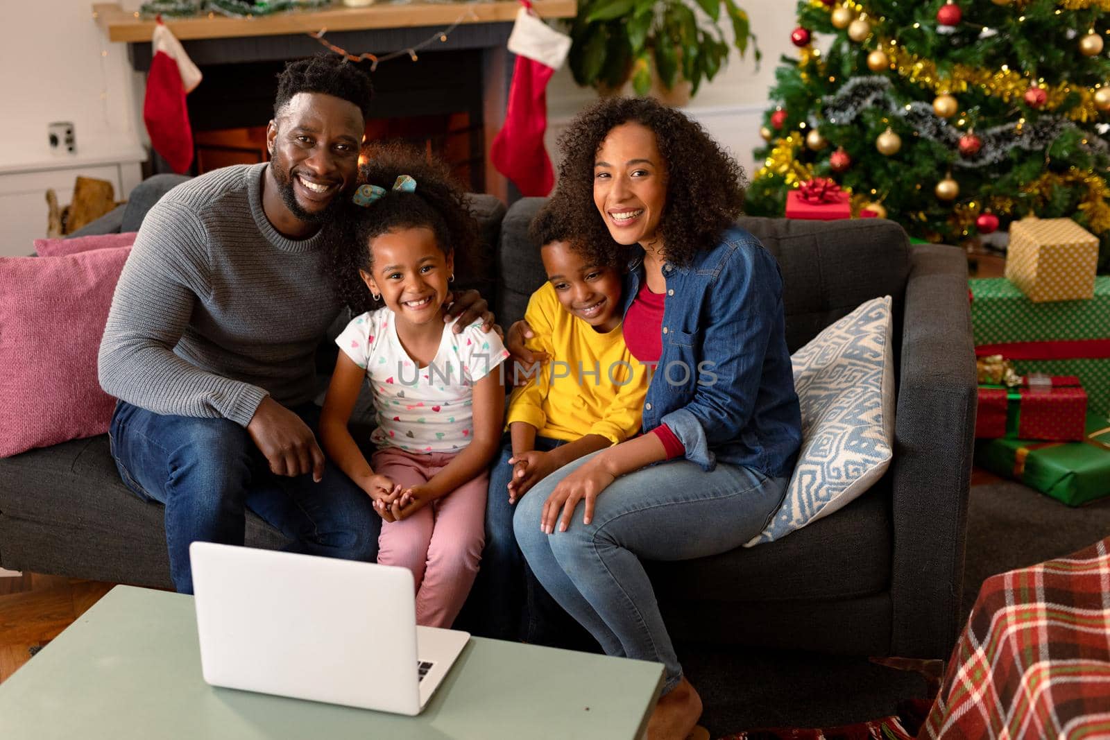 Happy african american family having video call on laptop, christmas decorations in background. christmas, festivity and communication technology.
