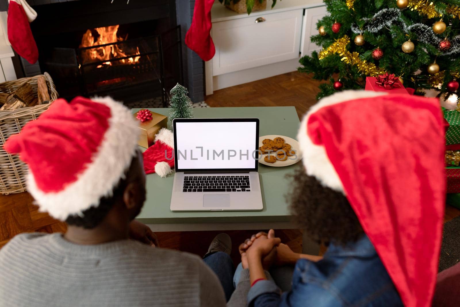 Back view of african american couple wearing santa hats, using laptop with copy space on screen. christmas, festivity and communication technology.