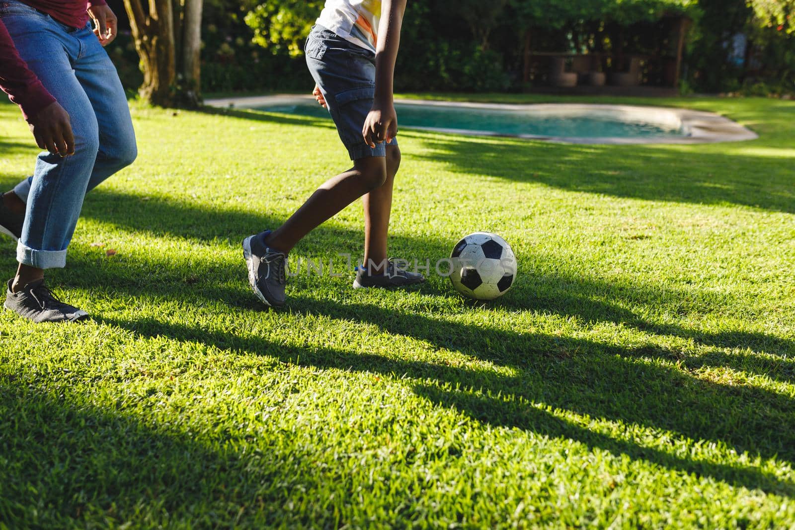 African american father with son having fun and playing football in garden. family spending time at home.