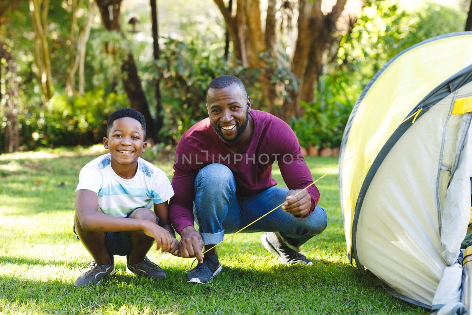 Portrait of african american father with son having fun and pitching tent in garden. family spending time at home.