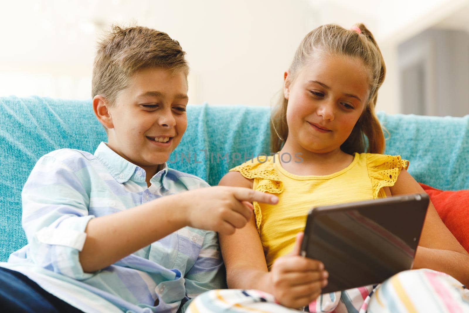 Happy caucasian brother and sister sitting on couch and using tablet in living room by Wavebreakmedia