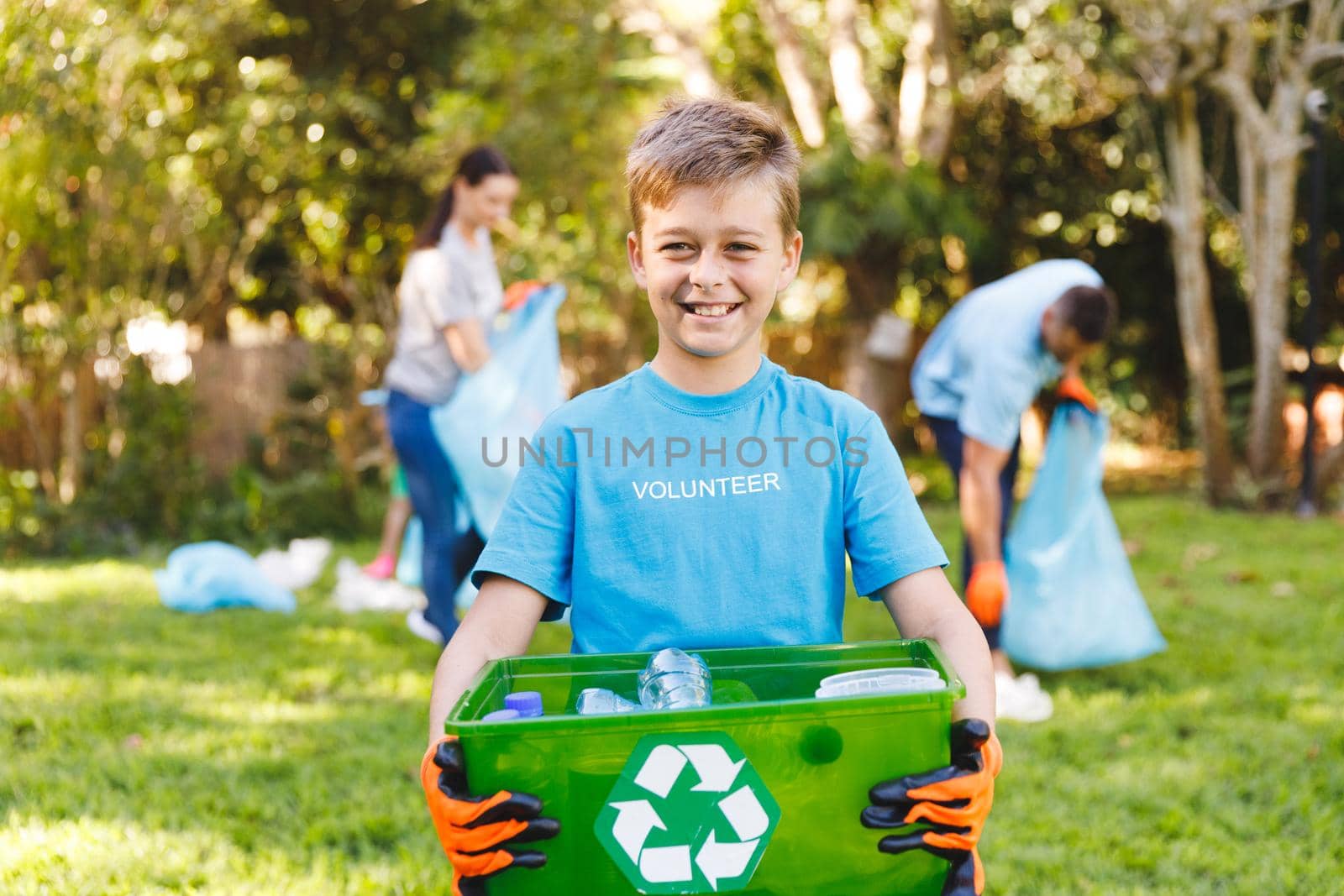 Portrait of smiling caucasian son holding recycling box, cleaning up countryside with parents. eco conservation volunteers, countryside clean-up.