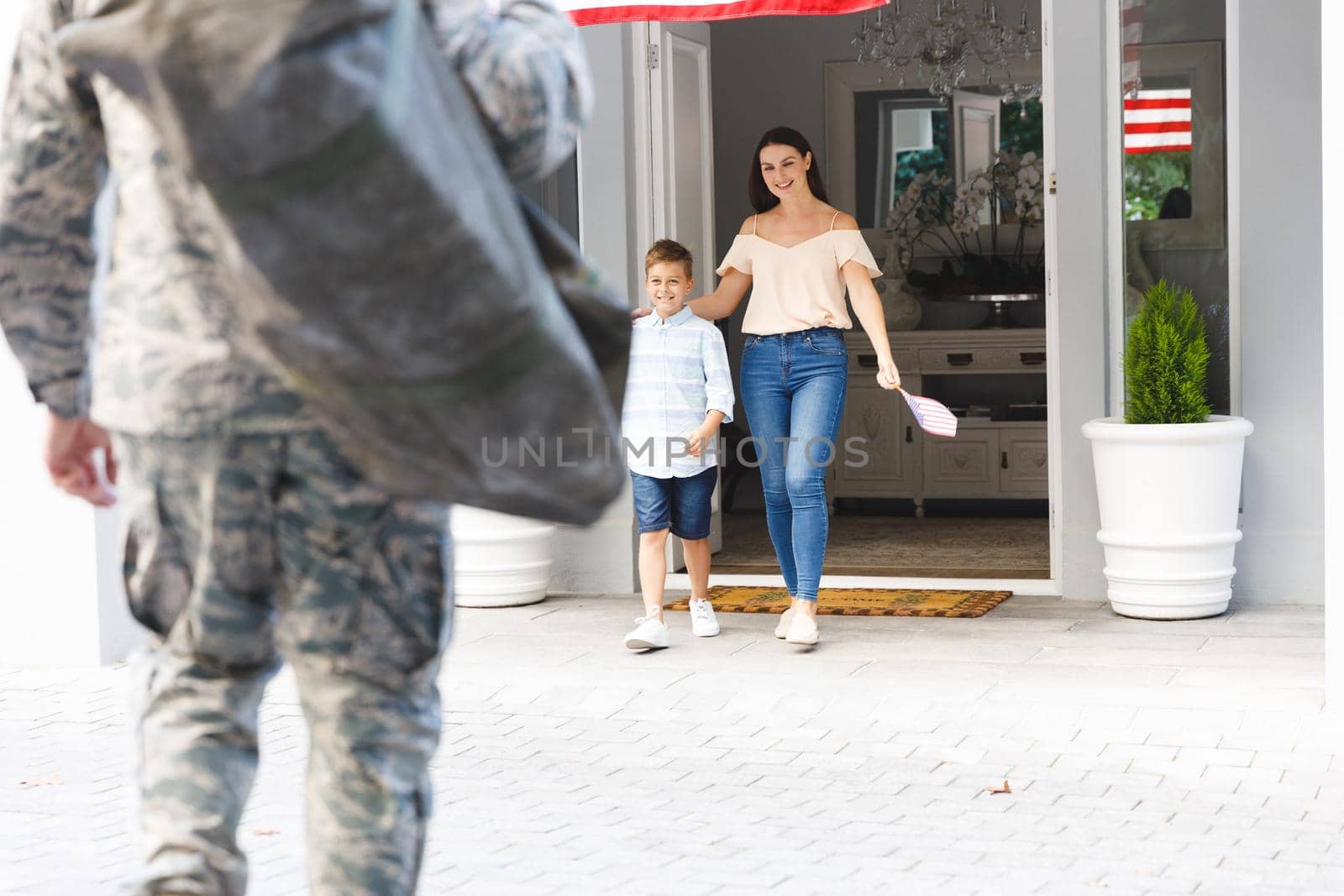 Caucasian male soldier with son and wife outside house decorated with american flag. soldier returning home to family.