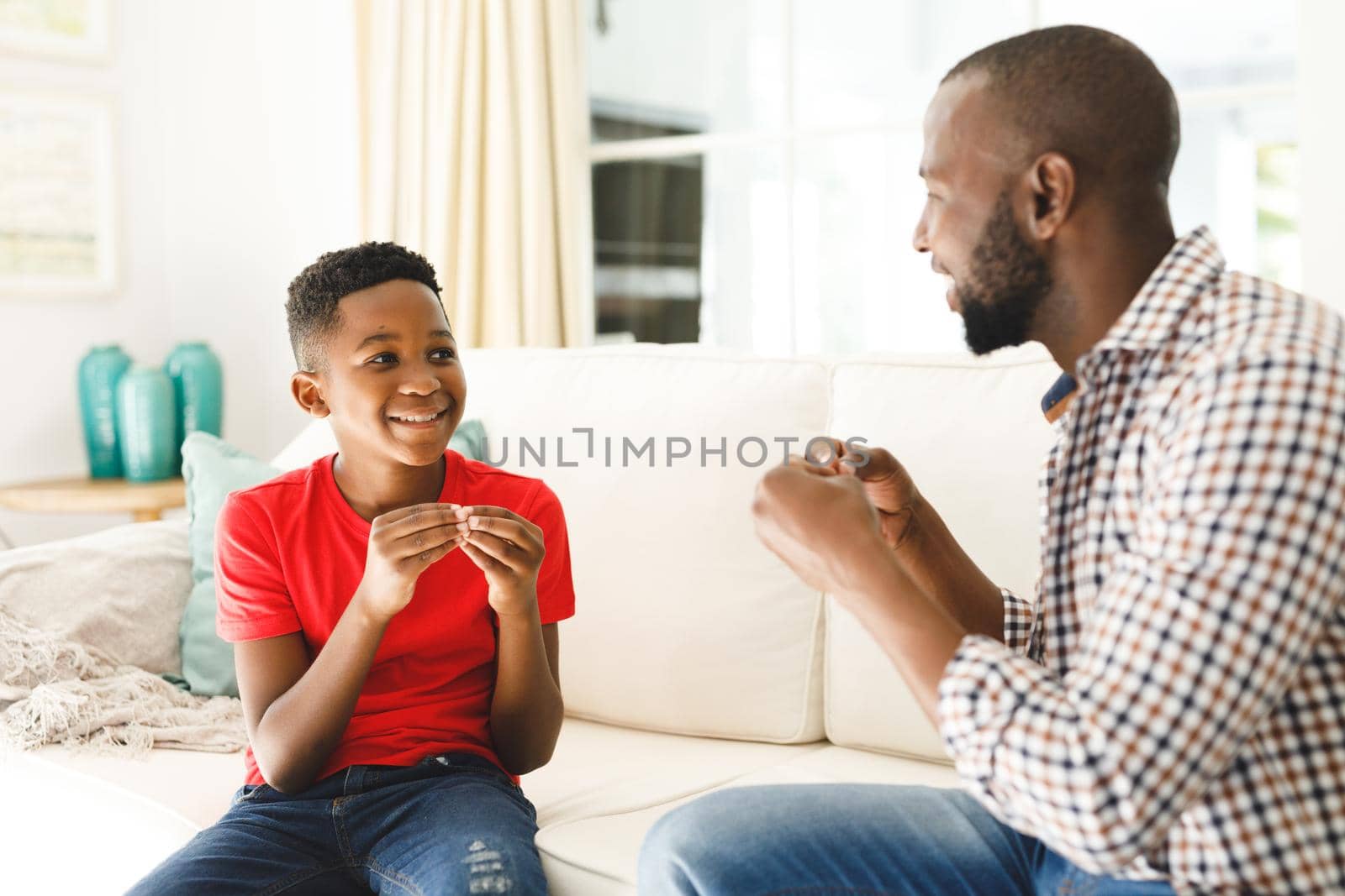 Happy african american father with son sitting on couch in living room talking sign language. father and son communicating without words.