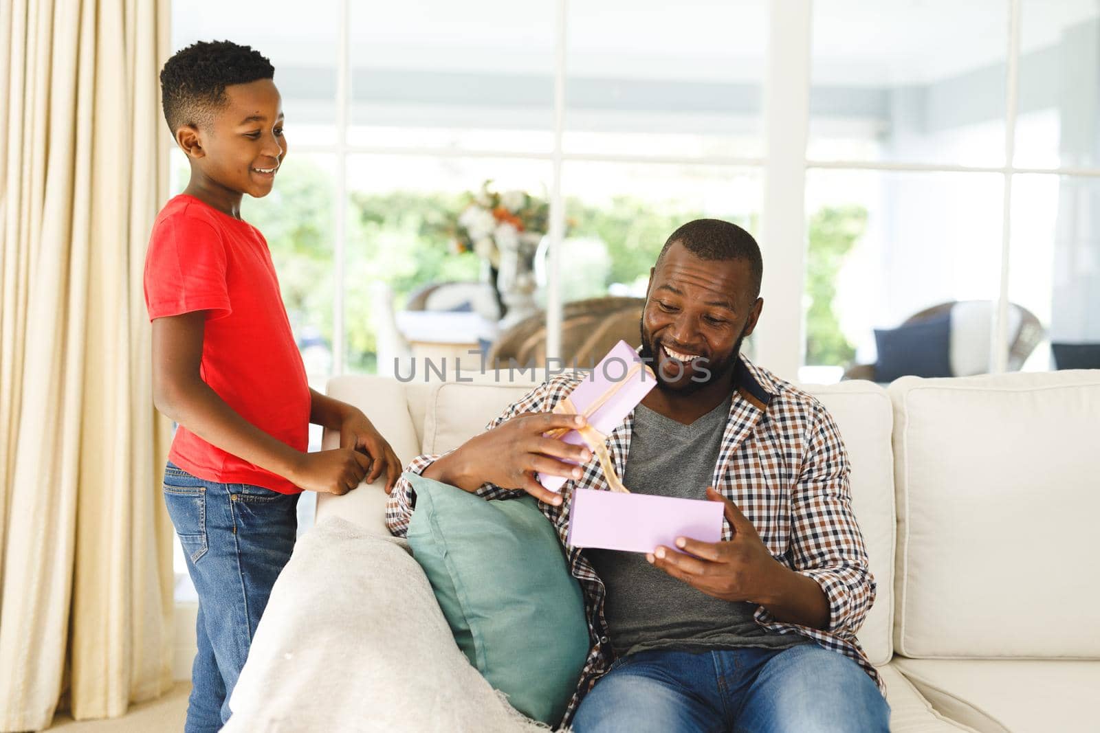 African american father opening gift from his son and smiling in living room by Wavebreakmedia