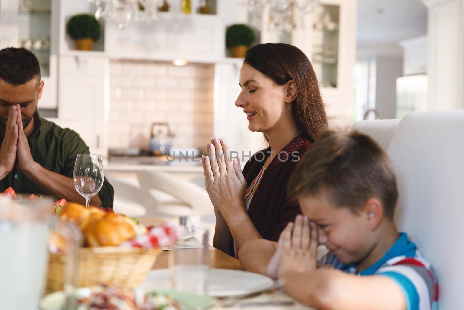 Caucasian parents with son sitting at table and praying before dinner. family enjoying traditional mealtime together at home.