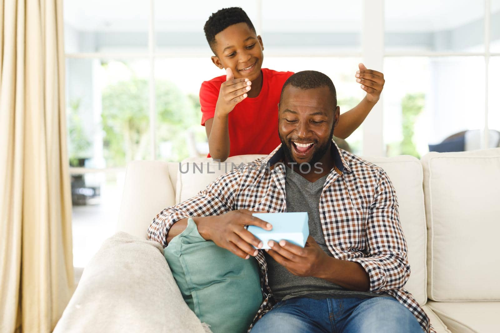 African american father opening gift from his son and smiling in living room by Wavebreakmedia
