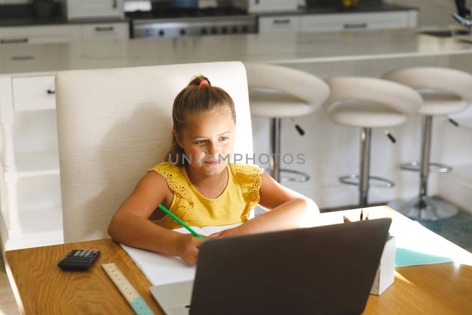 Caucasian girl sitting at table and using laptop during online lessons. childhood education and discovery at at home using technology.