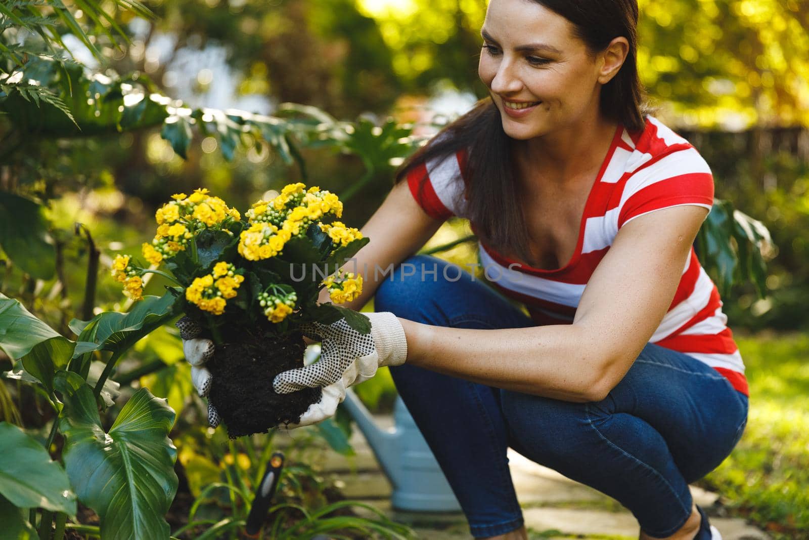 Smiling caucasian woman working in garden, holding flowers and wearing gloves. family enjoying leisure time together gardening at home.