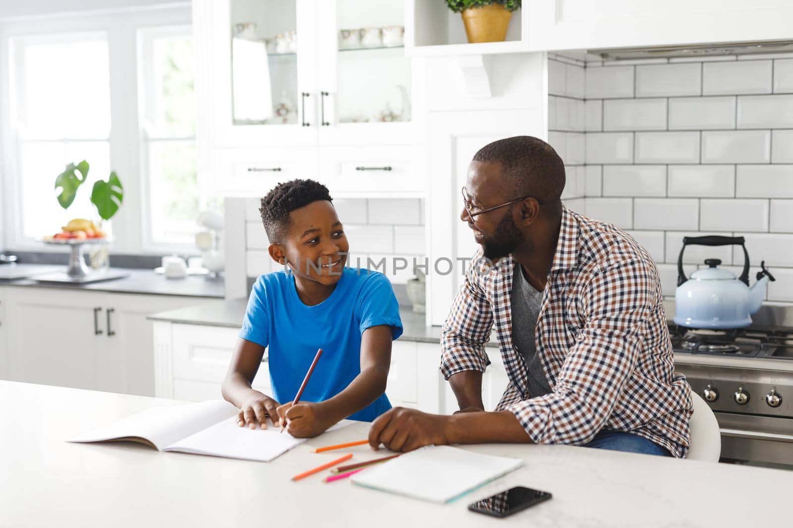Happy african american father and son in kitchen, doing homework together by Wavebreakmedia
