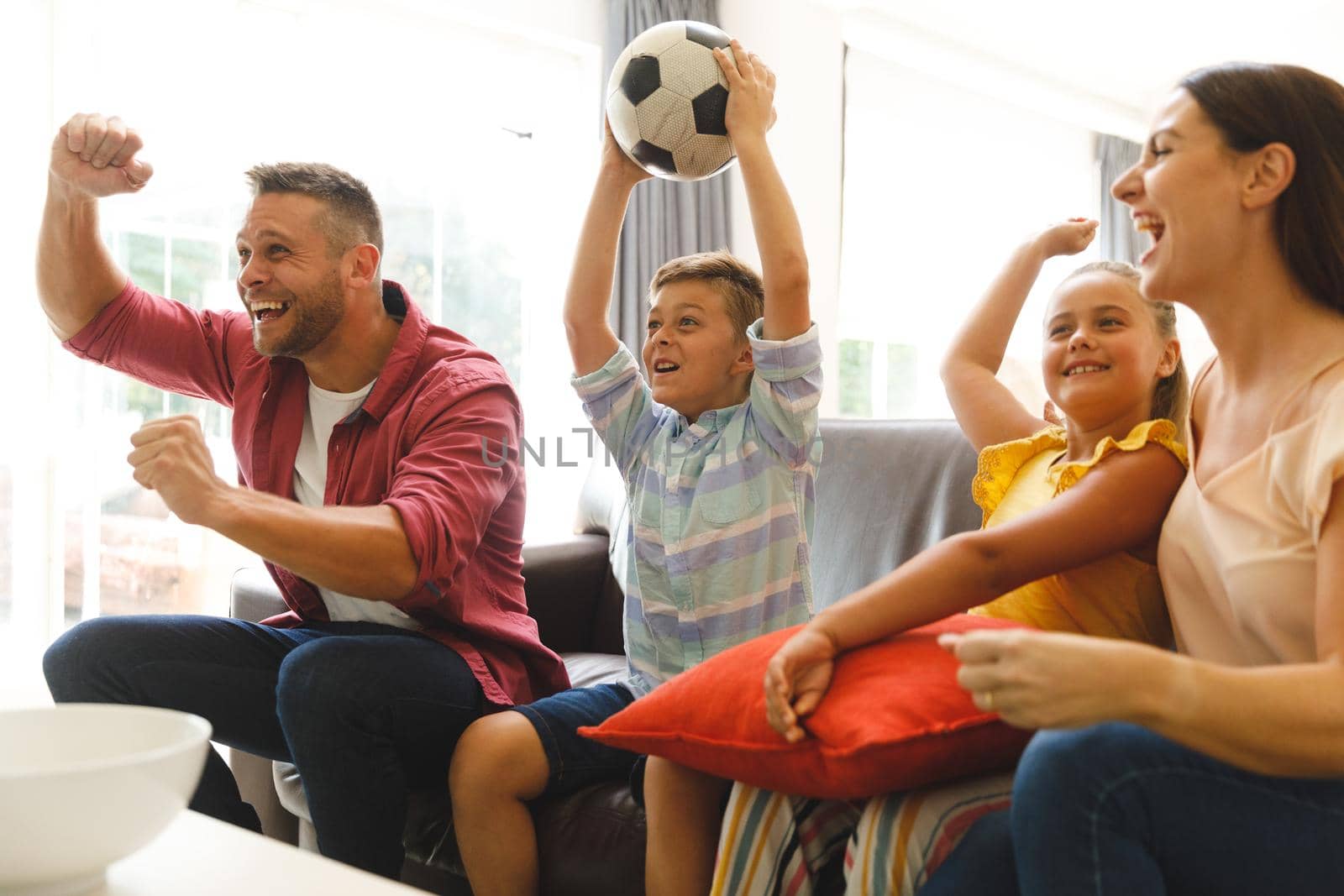 Excited caucasian parents on couch with daughter and son watching football match on tv and cheering. family entertainment and leisure time together at home.