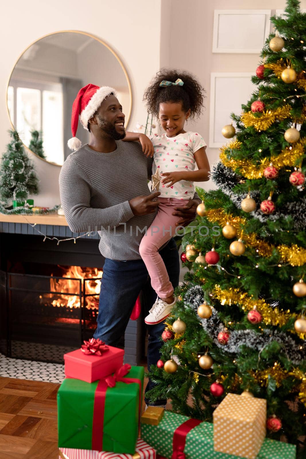 Happy african american father wearing santa hat and daughter decorating christmas tree. christmas, festivity and tradition at home.