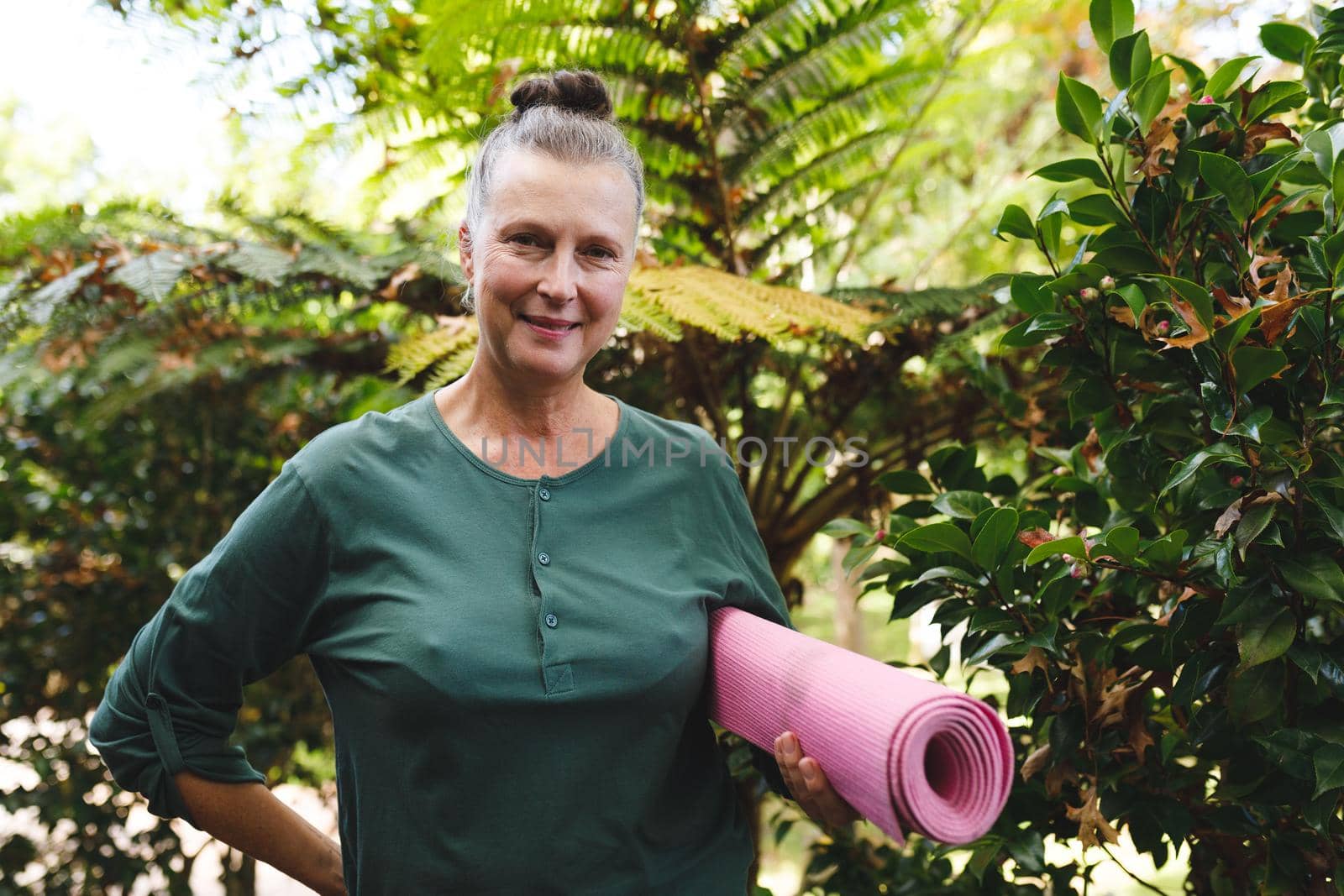 Portrait of happy senior caucasian woman holding yoga mat, looking to camera in sunny garden. healthy retirement lifestyle, spending time at home.
